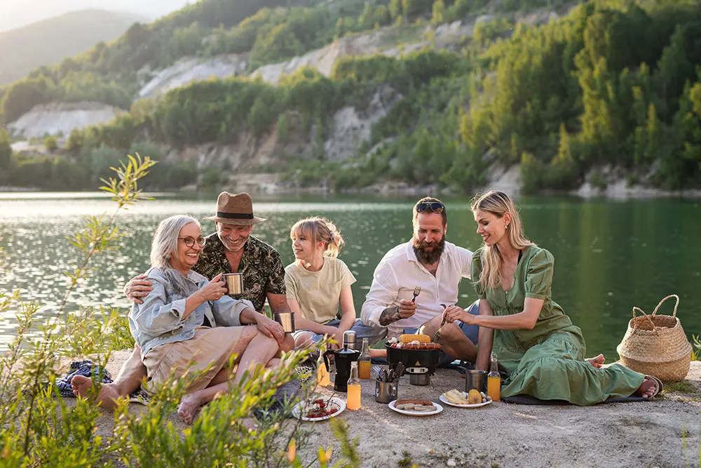 Happy multigeneration family eating meal by lake.