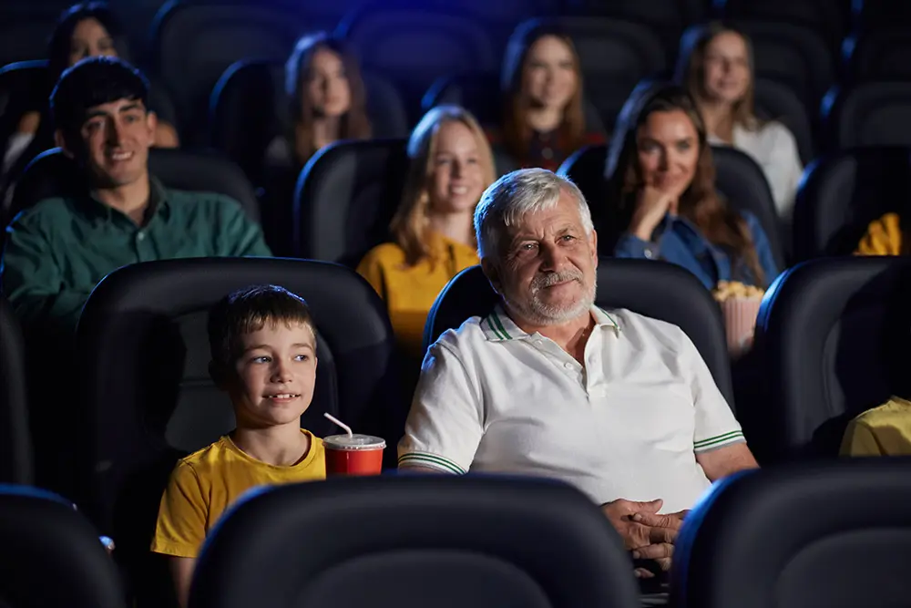 man and grandchild watching movie in busy theater