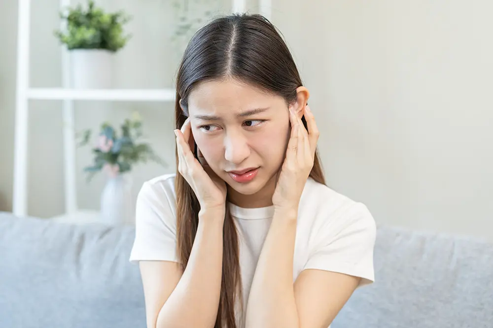 young woman holding ears suffering from Tinnitus