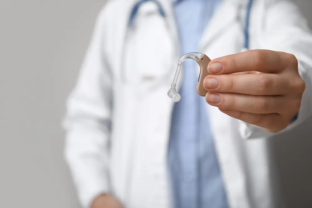 doctor holding hearing aid against grey wall, closeup